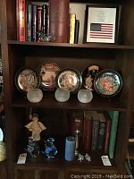 Four collector plates on stands with detailed scenes and frosted glass candle holders below them.