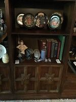 Photo showing contents on middle and lower shelves of the bookcase, including decorative plates, books, glassware, and miscellaneous collectibles, to illustrate the bookcase structure. Contents are not included.