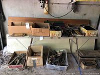 Multiple cardboard boxes and toolboxes on a folding table and on the floor containing assorted hand tools