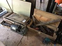 Two large wooden military ammunition mortar boxes with assorted tools inside on concrete floor.