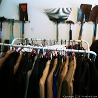 Close view of white metal clothing rack with hanging coats and jackets, showcasing rack structure and wheels for mobility.