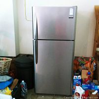 Full view of stainless steel refrigerator freezer in closed position with visible handles and surrounding items.