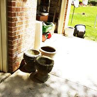 Two concrete Grecian urn style planter pots with classical shape and handles, placed outdoors near brick wall.