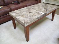 View of marble coffee table showing patterned marble top and wood legs beside brown leather couch.