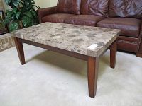 Full view of rectangular marble coffee table with wooden legs in front of a brown leather sofa, showing the polished marble surface and structure.