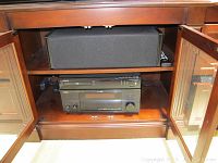 Open cabinet showing center speaker on upper shelf and electronics below