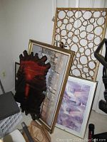 Multiple framed and unframed art pieces leaning against wall including dark wooden resin frame with red and sunset painting, 28x40 painting on canvas, framed print with flowers