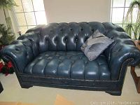 Full front view of dark blue tufted leather loveseat