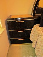 Black nightstand with three drawers and gold-tone handles, showing closed front.