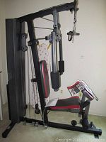 Side view of the home gym showing padded seat, backrest with red and black vinyl, and weight stack enclosed in black metal casing.