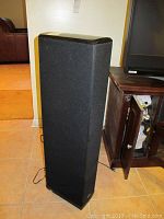 Front view of one tall speaker showing fabric grille and cabinet shape
