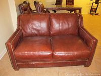 Front view of brown leather loveseat with nailhead trim, showing seat and back cushions