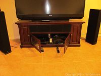 Front view of wooden entertainment center with TV on top, both middle glass doors open showing electronics storage.
