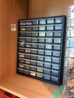 Full view of large black plastic storage case filled with 60 transparent drawers containing assorted beads of different colors and types.