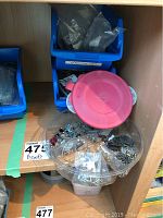 Four plastic containers filled with assorted beads and jewelry accessories. One container has a red lid. Assorted metal and glass beads visible.