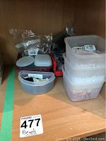 Image shows six plastic containers holding various beads and jewelry accessories on a wooden shelf.