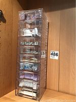 Full view of clear plastic tower with 10 drawers containing beads and accessories against wooden background