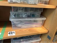 Three stacked plastic containers on a shelf holding beads and craft materials.