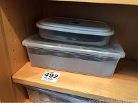 Two stacked plastic containers on a wooden shelf, displaying the lot contents stored within clear containers.
