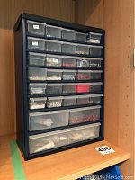 Full view of dark blue plastic storage unit with 33 clear drawers containing beads and jewelry supplies, side angle view
