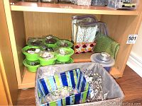 Green segmented containers holding assorted beads and clear plastic bags with beads and jewellery pieces inside a wooden shelf