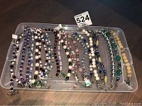 Top-down view of a plastic tray containing over 20 beaded costume jewellery bracelets in various colors and designs featuring purple, blue, pearl-like, pink, and turquoise beads.
