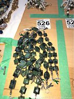 Bracelets laid out on a table showing various green stones connected with silver-tone beads and toggle clasps, with green ribbon charms attached.