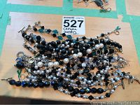 Close up photo showing a tangled pile of bracelets with black beads, white faux pearls, and metallic clasps.
