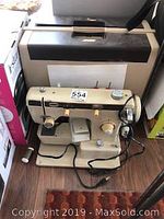 Overall view of Eaton zigzag stitch sewing machine next to case, showing machine's beige body, power cord, and foot pedal.