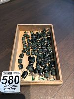 Photo showing a wooden box with seven green and black marbled stone bracelets with silver clasps laid out inside.