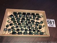 Nine green and black rectangular and square stone bead bracelets laid out in a box, showing overall quantity and design features.
