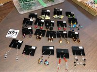 Nineteen pairs of costume earrings arranged on a table, each mounted on black display cards with price tags visible.