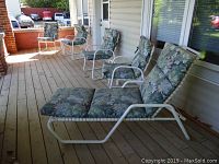 Four aluminium patio chairs with floral cushions lined up on porch deck.