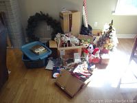 Wide view showing entire lot including storage bin, wreath leaning on wall, two decorated artificial Christmas trees and assorted boxes with decorations