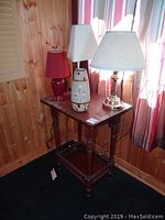 Full view of wooden side table with three lamps and decorative vase on top, showing overall condition including wood wear and stains.