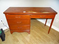Solid wood desk, reddish brown finish, showing age wear on top surface and four drawers with wood handles.