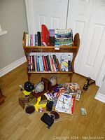 Full view of wooden bookshelf with books on two shelves, several items such as bookends, office supplies and a desk lamp arranged on floor in front of the bookshelf