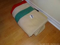 Folded wool blanket showing cream base and red, green stripe accents