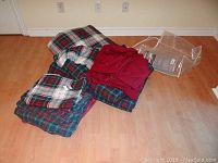Two folded plaid comforters in red, green, blue, and white with some solid red fabric and packaging visible on the floor.