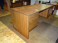 Wood office desk with drawers and locking keys visible on drawer handles, medium brown wood grain finish.