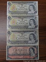 Top down image showing three 1973 one dollar bills and one 1954 two dollar bill all featuring Queen Elizabeth II and Canadian insignias