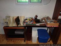 The metal frame table with dark surface and lower shelf, beige file folder organizers, assorted office supplies and storage bins underneath.
