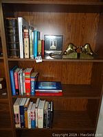 Bookshelf with multiple books including an old Bible, Norman Rockwell's America book, and other assorted books along with brass bull bookends.