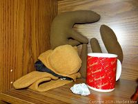 Photo showing brown plush toy, red travel mug with 'Bah Humbug!' text, and a light blue gemstone on wooden shelf.