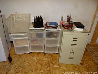 Photo shows metal two-drawer file cabinet, three plastic storage bins with drawers and casters, and office organizers on top including wire trays and pen holders.