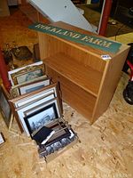 Two-tier wooden bookcase with assorted picture frames placed in front on the floor.