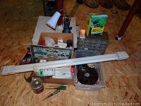 Photo showing collection of various hardware items including storage bin, measuring tape, assorted light bulbs, fluorescent tube light, wire connectors, and insect traps box.