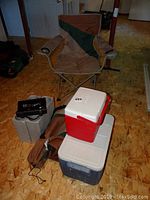 Two Coleman coolers stacked, two wine bottle coolers, black corkscrew set, and a folded camp chair in the background