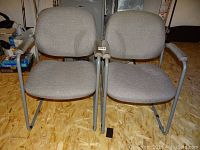Front view of two identical gray office chairs with metal frame, showing seat and back upholstery and armrests.