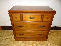 Front view of the three drawer wooden dresser showing medium brown finish and hardware.